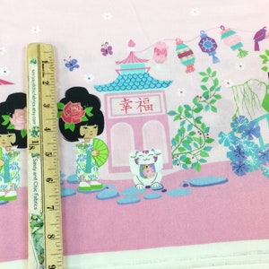 May include: Pink fabric with a Japanese-themed print. The design features cartoon geishas, pagodas, lucky cats, and floral elements. A wooden ruler is placed on the fabric, showing measurements in inches.