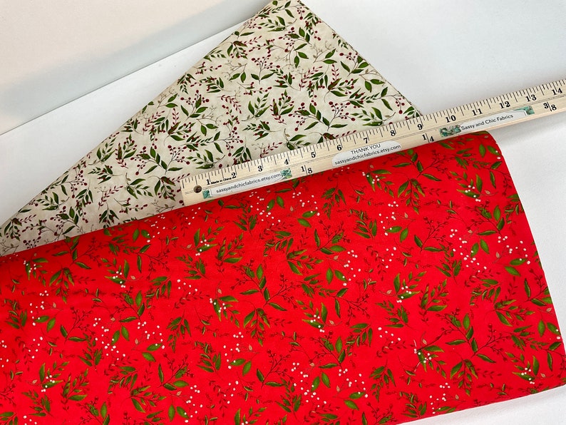 Puede incluir: Dos muestras de tela con estampados bot&aacute;nicos. Una es roja con hojas verdes y bayas blancas, la otra es crema con acentos verdes y rojos similares. Una regla con texto se coloca sobre las telas.