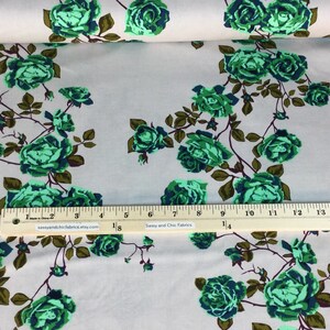 May include: Fabric with a floral pattern featuring green roses and dark green leaves on a light beige background. The fabric is printed with a ruler showing inches. The text "Sassy and Chic Fabrics" is printed on the ruler.