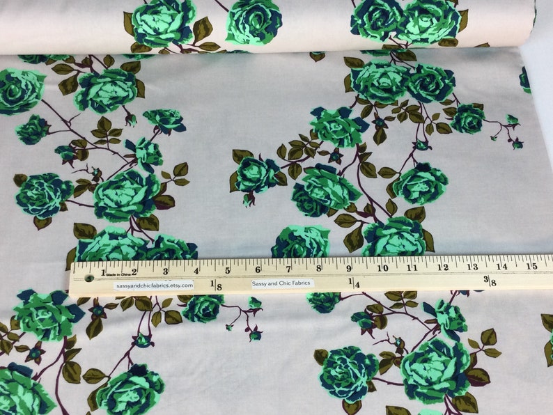 May include: Fabric with a floral pattern featuring green roses and dark green leaves on a light beige background. The fabric is printed with a ruler showing inches. The text "Sassy and Chic Fabrics" is printed on the ruler.