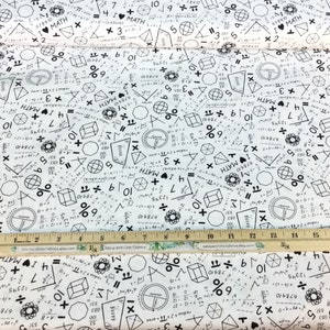 May include: White fabric printed with black math symbols, equations, and the phrase "I ❤️ MATH." Geometric shapes and numbers are scattered across the surface. A wooden ruler with inch markings is placed on the fabric.