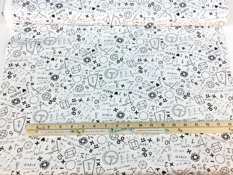 May include: White fabric printed with black math symbols, equations, and the phrase "I ❤️ MATH." Geometric shapes and numbers are scattered across the surface. A wooden ruler with inch markings is placed on the fabric.