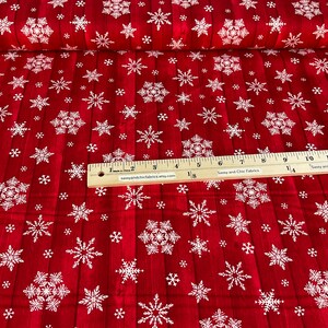 Pu&ograve; includere: Tessuto rosso con motivo a fiocchi di neve bianchi. Il tessuto presenta un effetto legno e un righello &egrave; posizionato sopra. Il testo "Sassy and Chic Fabrics" &egrave; visibile sul righello. Adatto per lavori creativi natalizi.