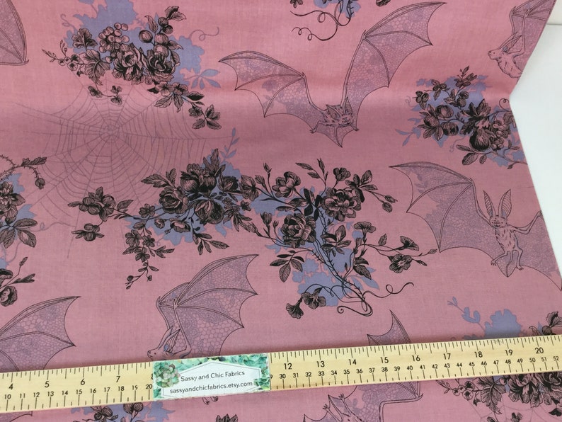 Puede incluir: Tela rosa con un patr&oacute;n repetido de murci&eacute;lagos, telara&ntilde;as y elementos florales en negro y morado claro. Medici&oacute;n en cent&iacute;metros.