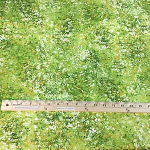 May include: Green fabric with a meadow-like pattern of white and yellow flowers. A wooden ruler with inch markings is placed on the fabric. The text "Sassy and Chic Fabrics" is visible on the ruler.