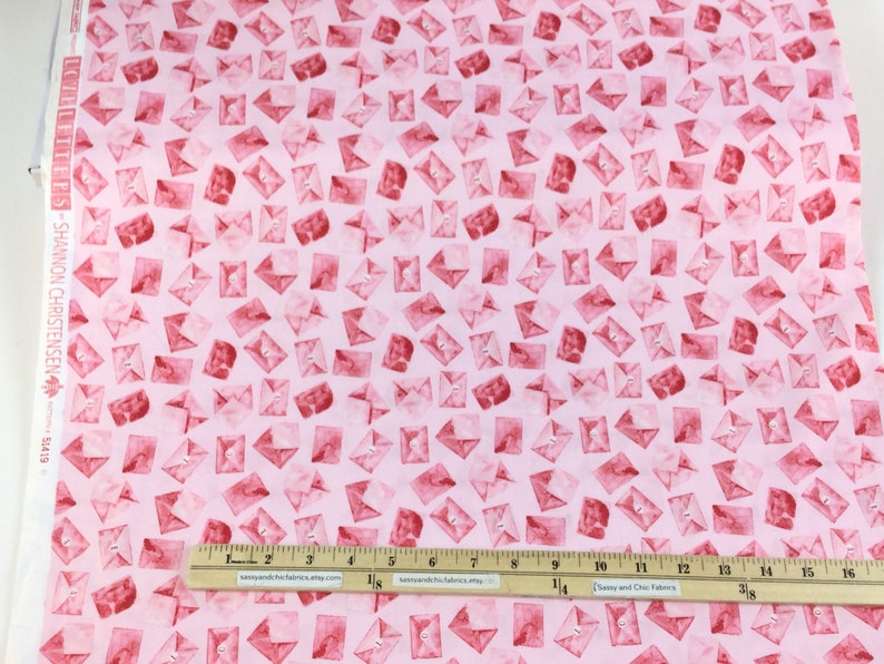 May include: Pink fabric with a repeating pattern of red watercolor envelopes. A ruler shows measurements in inches. The fabric is labeled "LETTERS - SHANNON CHRISTENSEN 51419".