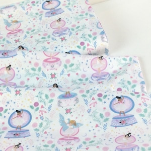 May include: White fabric with a repeating pattern of ballerinas inside snow globes, surrounded by flowers, stars, and crescent moons in pink, blue, and green. The fabric is folded, showing multiple layers of the printed design.