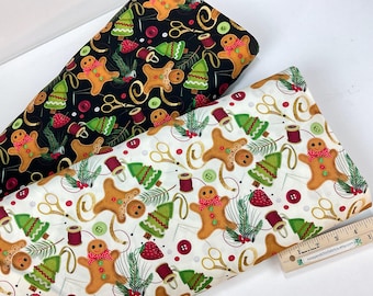 May include: Two fabric pieces with a Christmas theme. One is black with gingerbread men, Christmas trees, scissors, and buttons. The other is white with the same design. A ruler is visible.