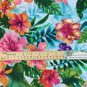 May include: Fabric with a tropical floral pattern featuring large hibiscus flowers in shades of pink, orange, and yellow, set against a light blue background with green leaves. A ruler shows measurements in inches.