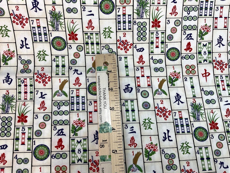 May include: Fabric with a repeating pattern of Mahjong tiles in cream, red, green, and black. The design includes Chinese characters, bamboo, flowers, and circles. A wooden ruler is placed on the fabric.