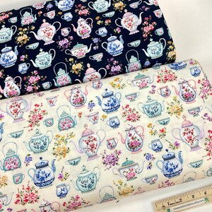 May include: Two rolls of fabric with a repeating pattern of teapots, teacups, and floral arrangements. One fabric is navy blue, the other is off-white. The teapots and cups are in pastel colors with floral designs.