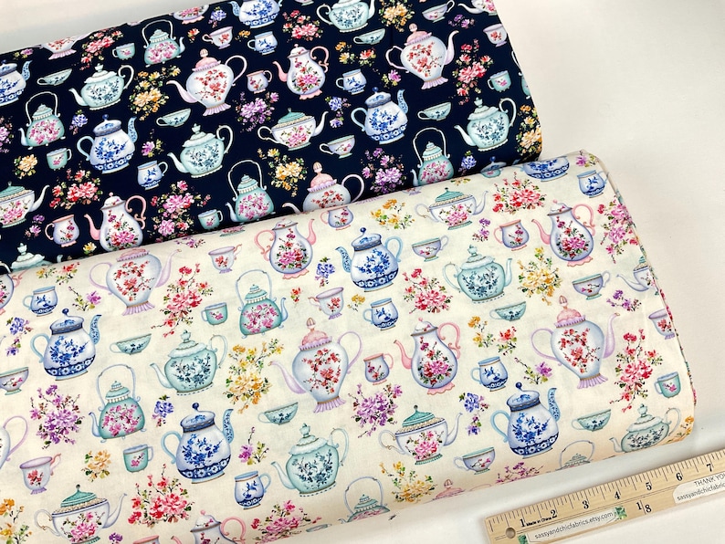 May include: Two rolls of fabric with a repeating pattern of teapots, teacups, and floral arrangements. One fabric is navy blue, the other is off-white. The teapots and cups are in pastel colors with floral designs.