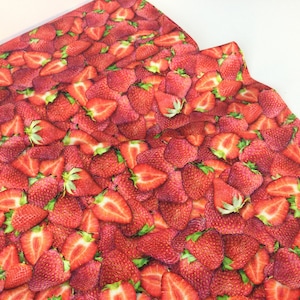 May include: A close-up of a fabric with a vibrant pattern of ripe strawberries. The design features whole and sliced strawberries in shades of red, with green leaves. The fabric is likely used for crafting or home decor.