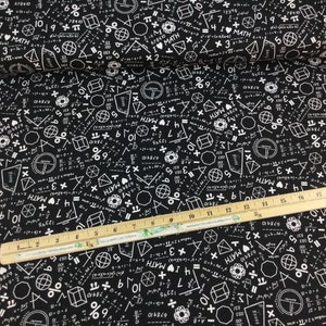 May include: Black fabric printed with white math symbols, equations, and the words "I MATH." Geometric shapes and numbers are scattered across the fabric. A wooden ruler with inch markings is placed on the fabric.