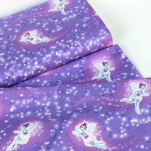 May include: Purple fabric with a repeating pattern of fairies with white wings and pink dresses. The fairies are surrounded by glowing orbs and sparkles. The fabric is folded, showing multiple layers.