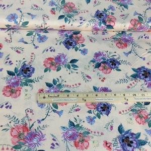 May include: Cream fabric with a floral design of pink, purple, and blue flowers. The fabric has a ruler along the bottom edge. The flowers are arranged in clusters with green leaves and stems.