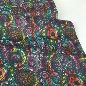 May include: Close-up of a fabric with a repeating mandala pattern. The design features concentric circles in shades of black, teal, pink, orange, and yellow. The fabric is folded, revealing layers of the patterned material.
