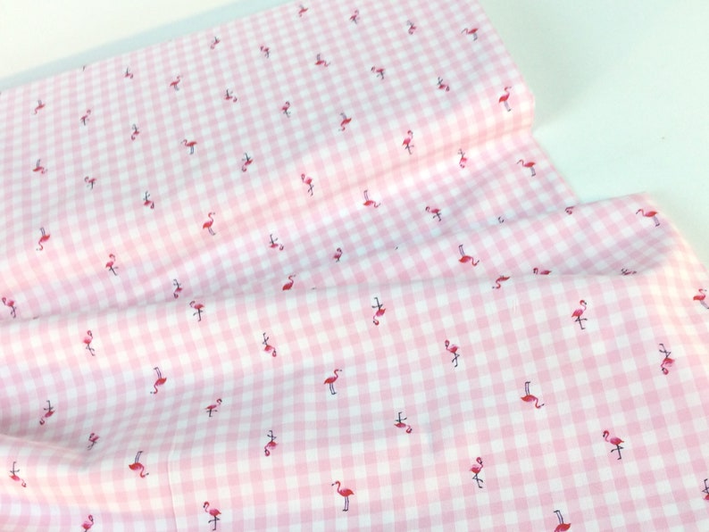 Puede incluir: Tela de cuadros rosa y blanco con un patr&oacute;n repetido de peque&ntilde;os flamencos rojos. La tela est&aacute; doblada, mostrando la textura y el patr&oacute;n del material. Ideal para proyectos de manualidades, costura o decoraci&oacute;n del hogar.