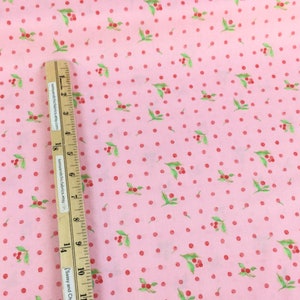 Puede incluir: Tela rosa con un estampado de lunares rojos y peque&ntilde;os grupos de bayas rojas con hojas verdes. Una regla de madera con medidas en cent&iacute;metros se coloca en diagonal sobre la tela.