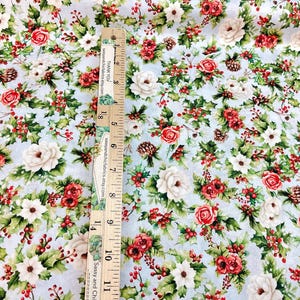 K&ouml;nnte beinhalten: Blumenstoff mit hellblauem Hintergrund, mit roten Rosen, wei&szlig;en Blumen, gr&uuml;nen Bl&auml;ttern und roten Beeren. Ein Holzlineal ist vertikal auf dem Stoff platziert. Auf dem Lineal steht "THANK YOU" und "Sassy and Chic Fabrics".