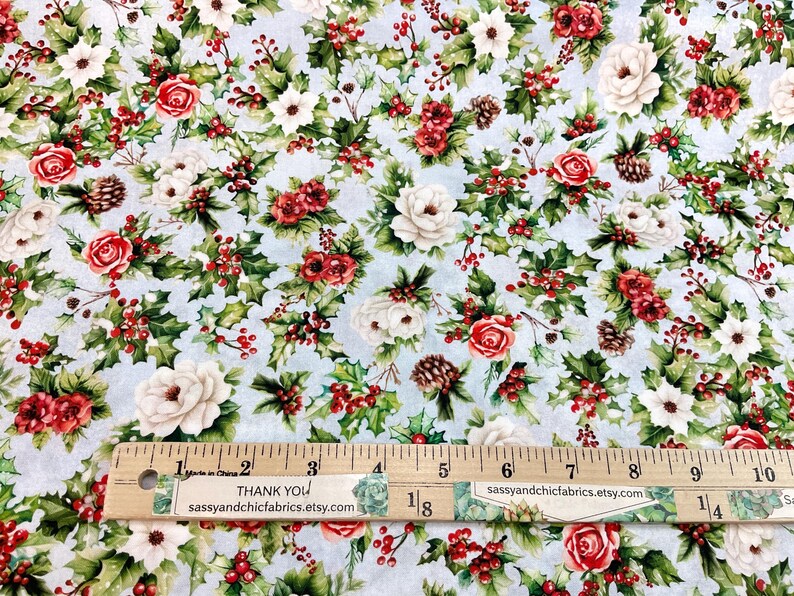 K&ouml;nnte beinhalten: Hellblauer Stoff mit einem Blumenmuster aus roten Rosen, wei&szlig;en Bl&uuml;ten, gr&uuml;nen Stechpalmenbl&auml;ttern und roten Beeren. Ein Holzlineal mit Zentimetermarkierungen und Text liegt auf dem Stoff. Der Text auf dem Lineal lautet "THANK YOU" und "sassyandchicfabrics.etsy.com".