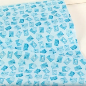 May include: Light blue fabric with a repeating pattern of watercolor-style envelopes. The envelopes are in varying shades of blue and have a button closure design. The fabric is likely cotton or a similar material, suitable for quilting or crafting projects.