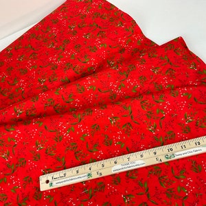 Puede incluir: Tela roja con un patr&oacute;n repetido de hojas verdes y peque&ntilde;os puntos blancos. Una regla de madera con medidas en cent&iacute;metros est&aacute; colocada sobre la tela. La tela est&aacute; doblada y parece ser de algod&oacute;n.