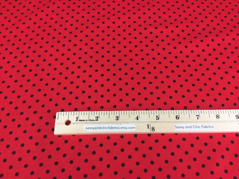May include: Red fabric with black polka dots. A wooden ruler with inch markings is placed across the fabric. The text "sassyandchicfabrics.etsy.com" is printed on the ruler.