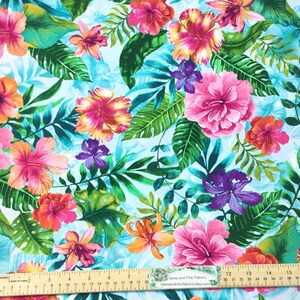 May include: Vibrant fabric featuring a tropical floral pattern. Large pink, orange, and yellow hibiscus flowers are interspersed with green leaves and purple orchids against a light blue background. A ruler is visible along the bottom edge.