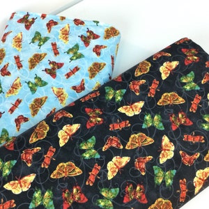 May include: Two fabric rolls with butterfly patterns. One is light blue with butterflies in yellow, green, and red. The other is dark blue with similar butterflies and a swirling design. Ideal for sewing and crafting.