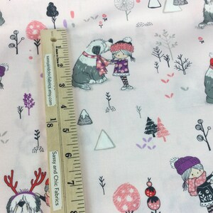 May include: Light pink fabric with a winter scene featuring cartoon dogs, children, trees, and snowmen. The dogs wear hats and scarves. The children wear hats, scarves, and dresses. The fabric has a ruler with the text "Sassy and Chic Fabrics etsy.com".