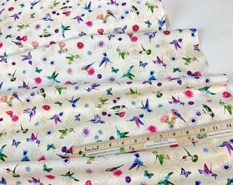 May include: Off-white fabric with a repeating pattern of hummingbirds, butterflies, and flowers in shades of blue, green, purple, and pink. The fabric also features a gold circular design. A ruler is visible.