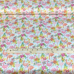 May include: A roll of fabric with a repeating pattern of pink and peach flamingos, yellow and orange flowers, and green leaves on a light blue background. A ruler with inch measurements is visible.