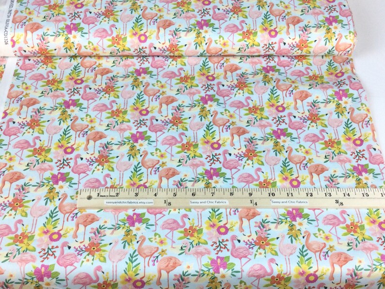 May include: A roll of fabric with a repeating pattern of pink and peach flamingos, yellow and orange flowers, and green leaves on a light blue background. A ruler with inch measurements is visible.