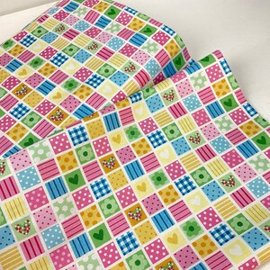 May include: A colorful fabric with a patchwork design. The pattern features squares in various colors, including pink, yellow, green, and blue. Each square contains hearts, flowers, polka dots, and stripes. The fabric is rolled up.