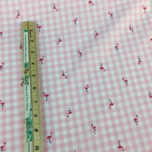 Puede incluir: Tela de cuadros rosa y blanco con un patr&oacute;n repetido de peque&ntilde;os flamencos rosas. Una regla de madera est&aacute; colocada sobre la tela, midiendo hasta 25 cm.