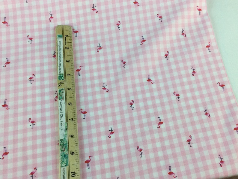 Puede incluir: Tela de cuadros rosa y blanco con un patr&oacute;n repetido de peque&ntilde;os flamencos rosas. Una regla de madera est&aacute; colocada sobre la tela, midiendo hasta 25 cm.