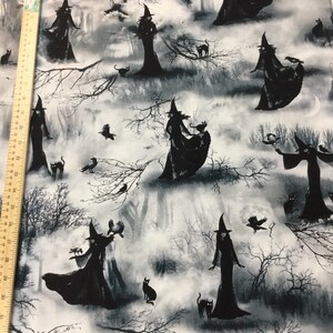 May include: Black and white fabric featuring a repeating pattern of witches in long dresses and pointed hats, with black cats, crows, and bare tree branches against a misty forest backdrop. The design has a spooky, Halloween theme.