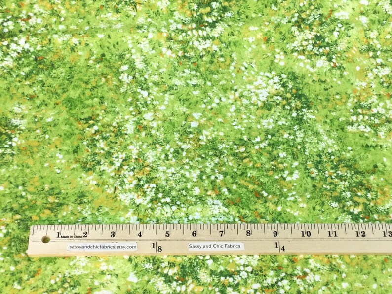 May include: Green fabric with a floral pattern featuring white and orange accents. The fabric has a ruler along the bottom edge, with the text "Sassy and Chic Fabrics" and the website address. The fabric is suitable for various sewing projects.