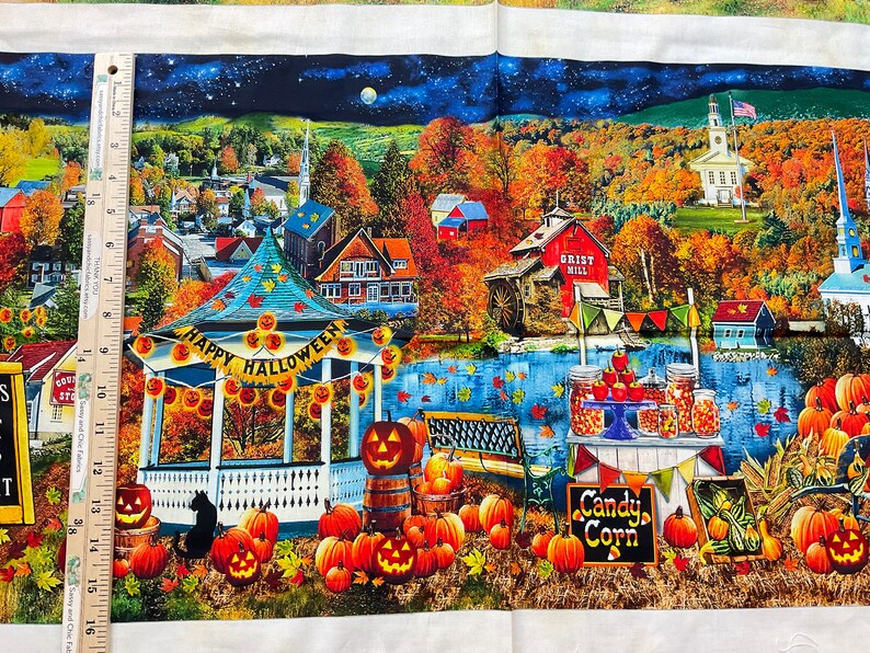 Op de afbeelding: Stoffpaneel met een feestelijke Halloween-sc&egrave;ne. Een prieel met een "Happy Halloween"-banner is omringd door pompoenen en een zwarte kat. De sc&egrave;ne omvat een stad, een molen en potten met snoepma&iuml;s. De nachthemel is zichtbaar.