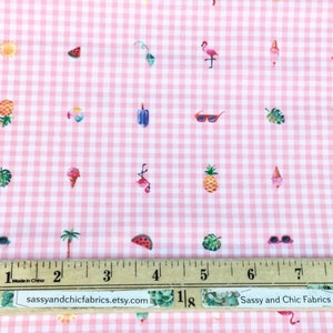 Puede incluir: Tela de cuadros rosa y blanco con un patr&oacute;n repetido de ilustraciones de verano. El dise&ntilde;o incluye pi&ntilde;as, helados, gafas de sol, flamencos y rodajas de sand&iacute;a. Una regla est&aacute; colocada sobre la tela. El texto "Sassy and Chic Fabrics" es visible.