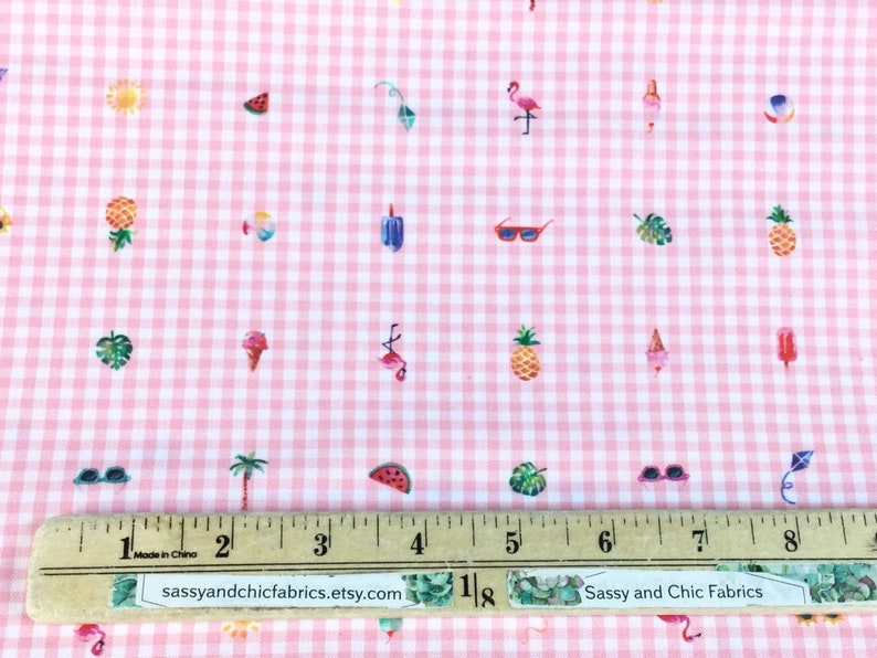 Puede incluir: Tela de cuadros rosa y blanco con un patr&oacute;n repetido de ilustraciones de verano. El dise&ntilde;o incluye pi&ntilde;as, helados, gafas de sol, flamencos y rodajas de sand&iacute;a. Una regla est&aacute; colocada sobre la tela. El texto "Sassy and Chic Fabrics" es visible.