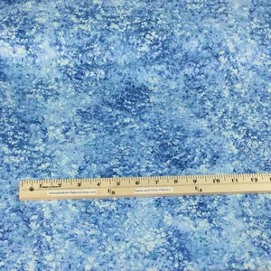 May include: Blue fabric with a white floral pattern. A wooden ruler with inch markings is placed across the fabric. The fabric has a watercolor effect with shades of blue and white. The text "Sassy and Chic Fabrics" is printed on the ruler.