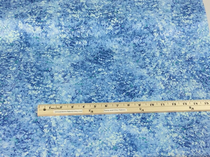 May include: Blue fabric with a white floral pattern. A wooden ruler with inch markings is placed across the fabric. The fabric has a watercolor effect with shades of blue and white. The text "Sassy and Chic Fabrics" is printed on the ruler.