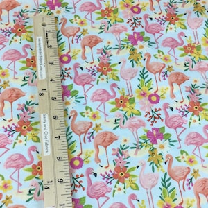 May include: Fabric with a repeating pattern of pink flamingos and colorful flowers on a light blue background. A wooden ruler with the text "Sassy and Chic Fabrics" is in the image.
