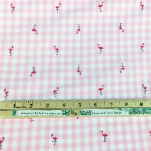 Puede incluir: Tela de cuadros rosa y blanco con un patr&oacute;n repetido de flamencos rosas. Una regla con pulgadas y el texto "Sassy and Chic Fabrics" son visibles en la tela.