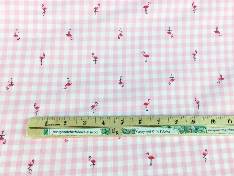 Puede incluir: Tela de cuadros rosa y blanco con un patr&oacute;n repetido de flamencos rosas. Una regla con pulgadas y el texto "Sassy and Chic Fabrics" son visibles en la tela.