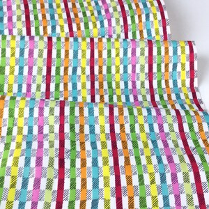 May include: Colorful fabric with a repeating pattern of vertical stripes and checkered blocks. The design features a vibrant mix of colors including red, orange, yellow, green, blue, and pink on a white background. The fabric is folded, showing multiple layers.