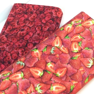 May include: Two fabric pieces with a fruit pattern. One features a dense arrangement of red raspberries, the other a mix of whole and sliced red strawberries. The fabrics have a bright, colorful appearance.