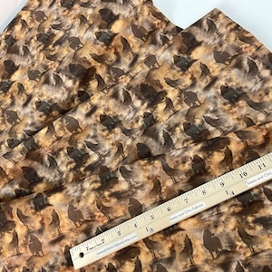 May include: Fabric with a repeating pattern of dark brown wolf silhouettes on a tan and brown mottled background. A ruler with inch measurements is placed across the fabric. The text "Sassy and Chic Fabrics" is visible on the ruler.